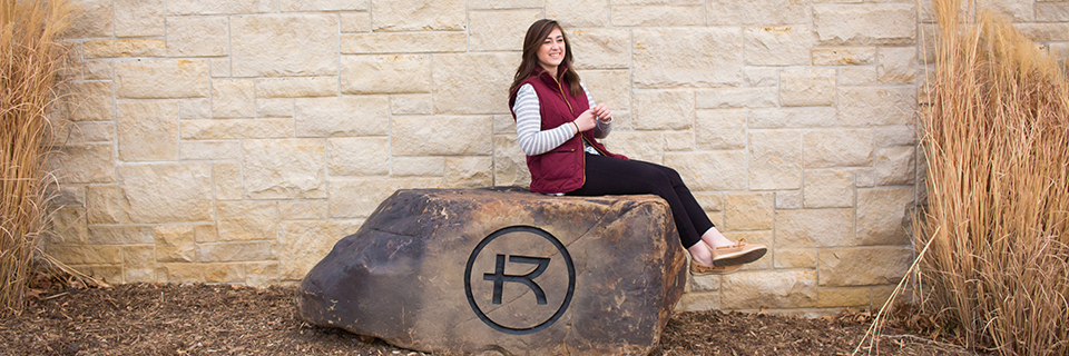 Gabby Brancato sitting on a rock stamped with the Rockhurst logo. 