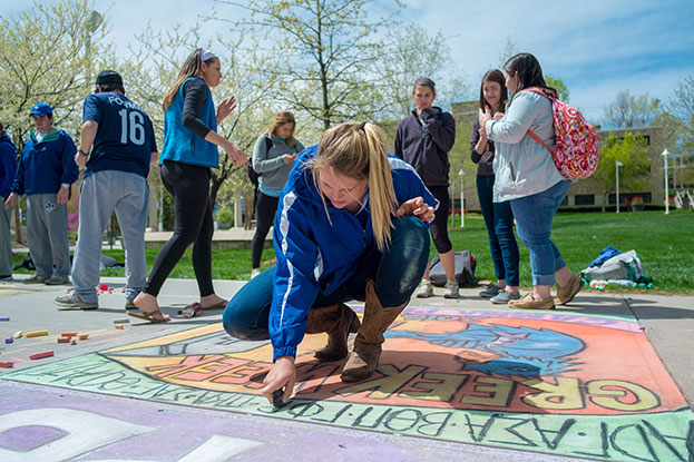 Meet the Greeks. Greek organization creating chalk drawings on the sidewalks of RU.