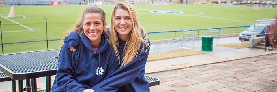 Lauren Merlo, '18, and Angela Merlo, '20 Angela and Lauren Merlo sit near the Rockhurst soccer field.