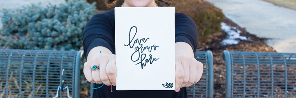 Sarah Hummel holds a canvas with the words "love grows here"