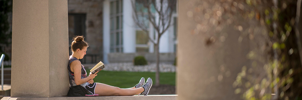 A student sits and reads in the Rockhurst pergola