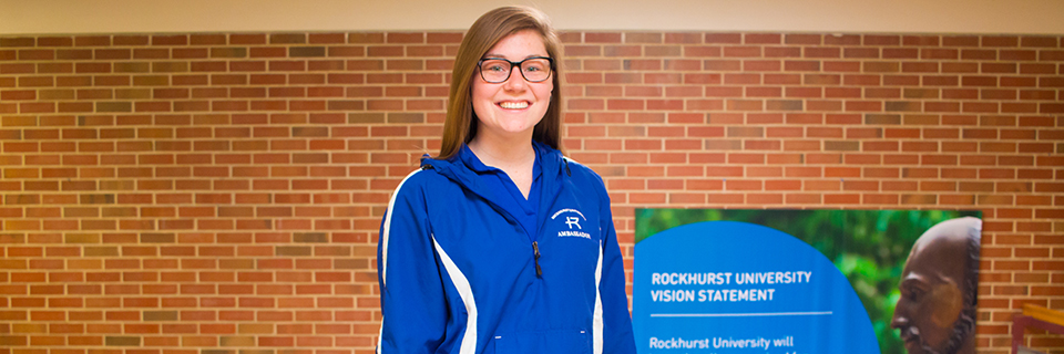 Sydney Hunter stands in front of a stairwell in Massman hall. 