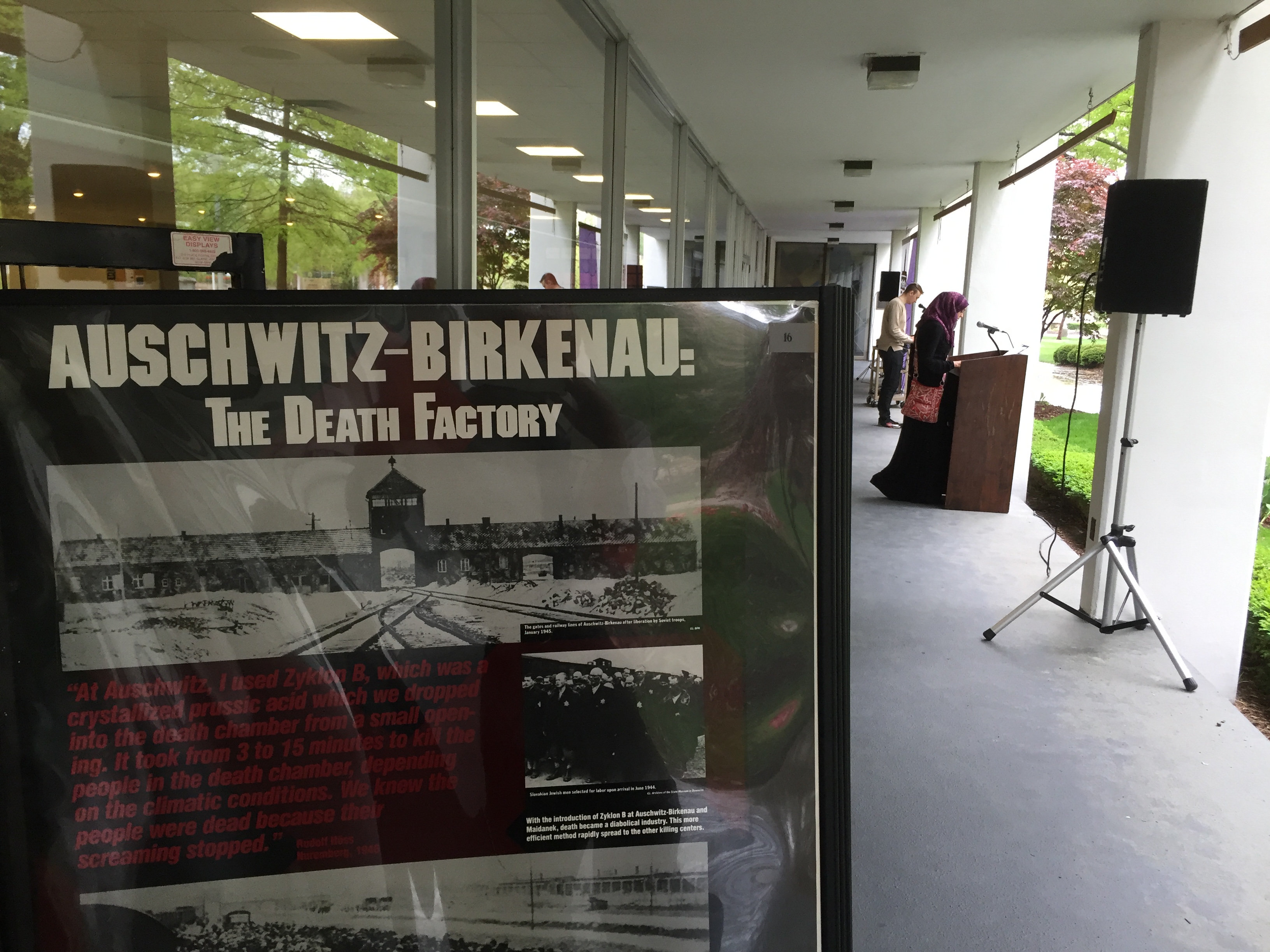 Auschwitz-Birkenau information poster in foreground; microphones on podiums with speakers in background