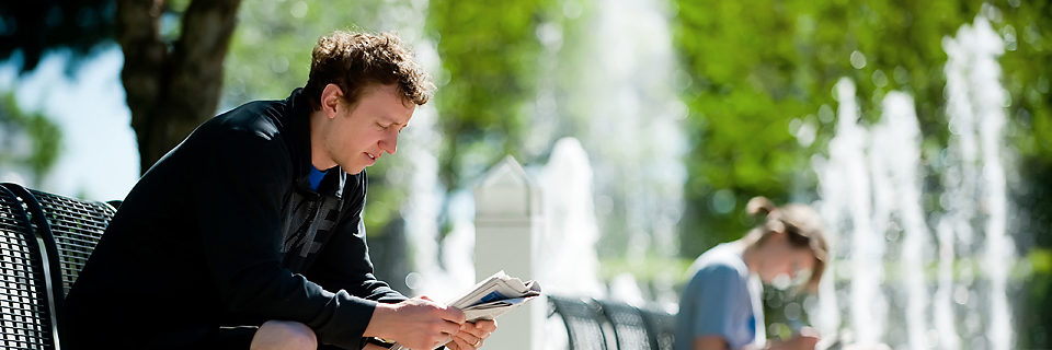 Criminal Justice Requirements Student reading by a fountain