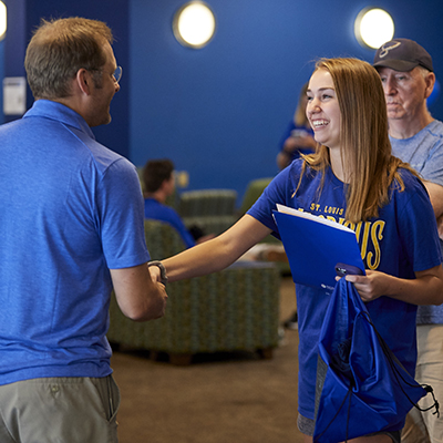 Bill Kriege shakes hands with a student as her father looks on