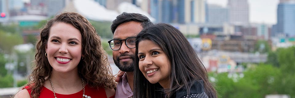 Three recent MBA graduates with Downtown KC in the background Stackable MBA now available at Rockhurst University, Kansas City