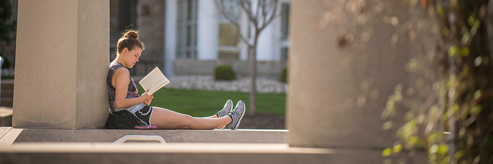 Student reads on ledge near pergola. 