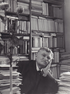 Gabriel Marcel sits at his desk, surrounded by piles of books
