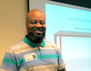Male teacher stands in front of a presentation screen