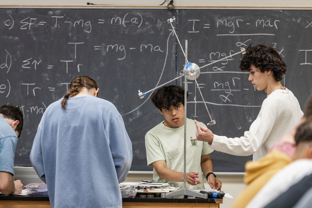 Students engage in a physics experiment with chalkboard in the background