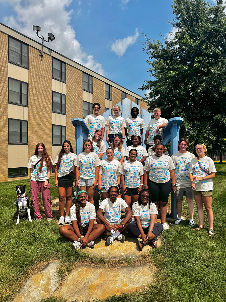 10 resident assistants pose for a group photo in the "Big Blue Chair." A dog sits next to them.