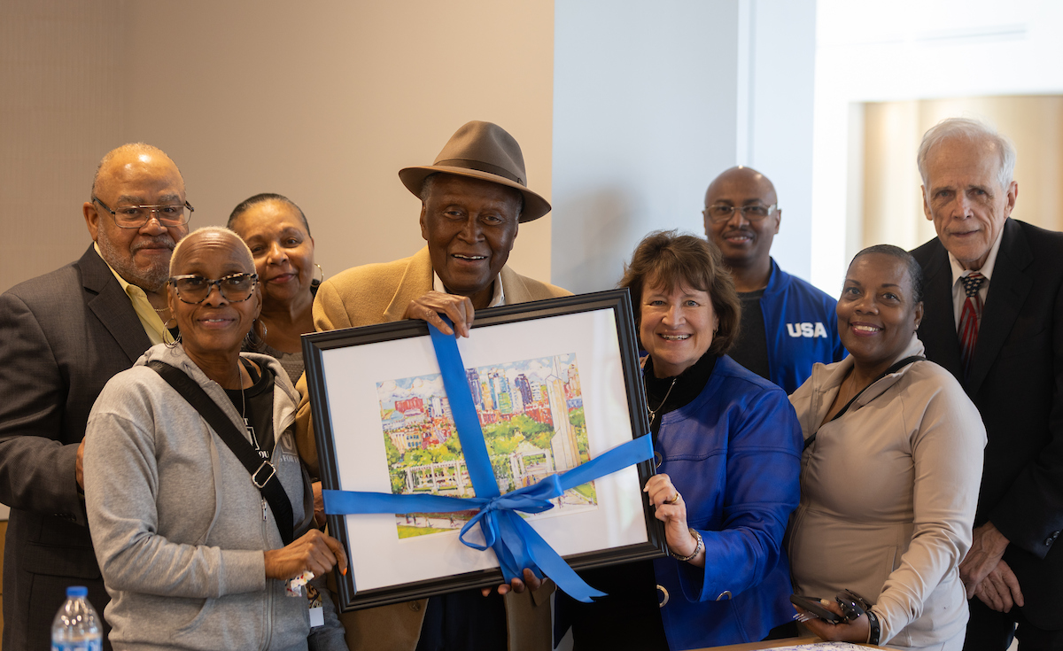 Alvin Brooks is surrounded by family, friends, and RU President Sandra Cassady. Brooks is holding a painting gift. 