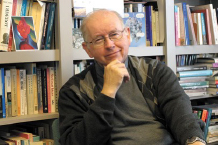 Thomas Flynn holds his hand to his chin with the backdrop of a bookshelf