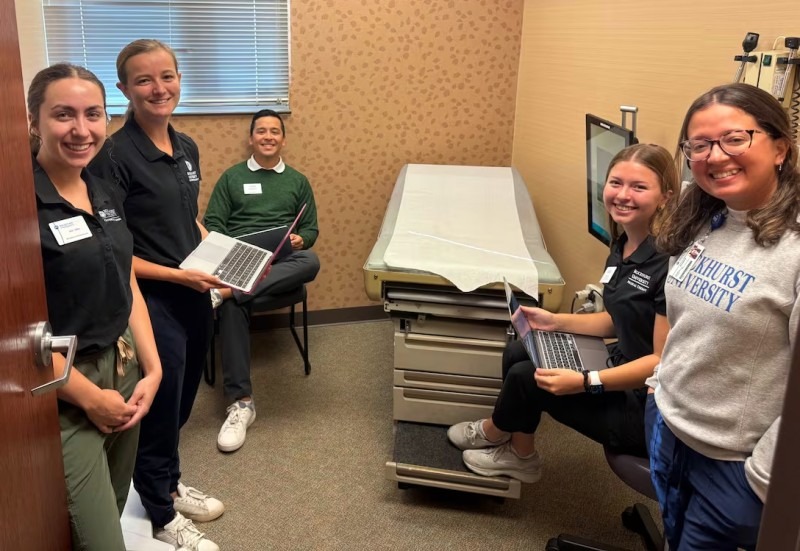 Five Rockhurst students sit in a medical room with an open patient chair/table