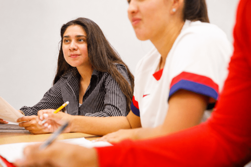 A female student smiles as she looks forward while sitting at a table in class