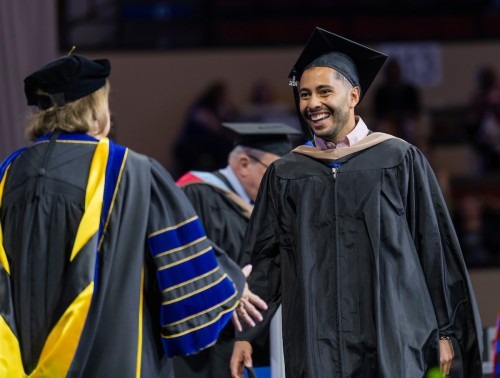 MBA grad smiles as he prepares to shake hands with Rockhurst President Sandra Cassady at Commencement 2024