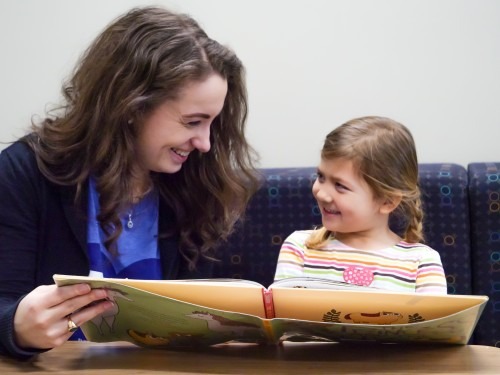 SLP student reading with child, exchanging smiles