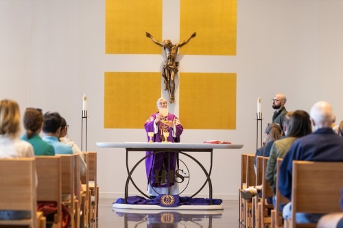 A priest celebrates Mass under a crucifix on the chapel wall