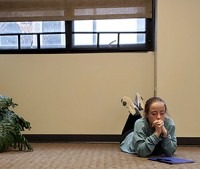 A girl lies on her stomach on the floor, praying 