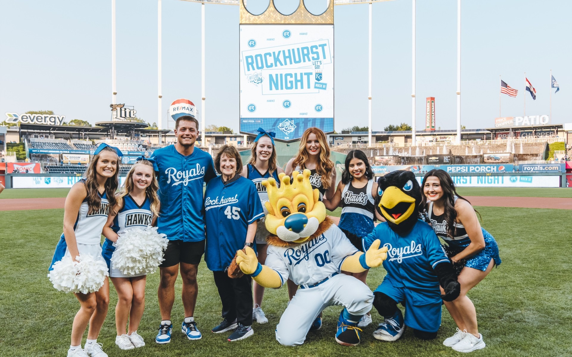 Rockhurst President Sandy Cassady, Rock E. Hawk, Slugerrr and Rockhurst students standing on field at Royals stadium