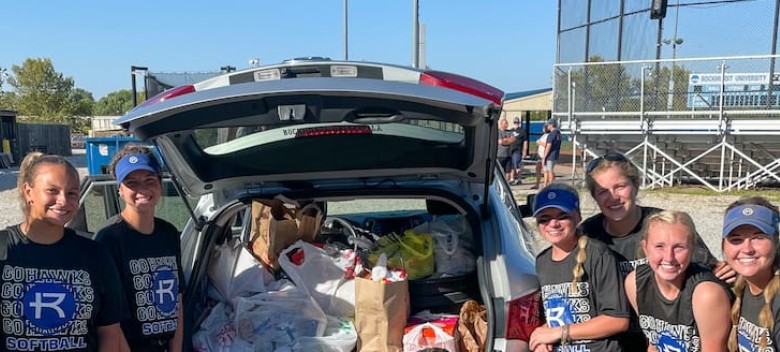 Softball players around a car trunk full of donations.