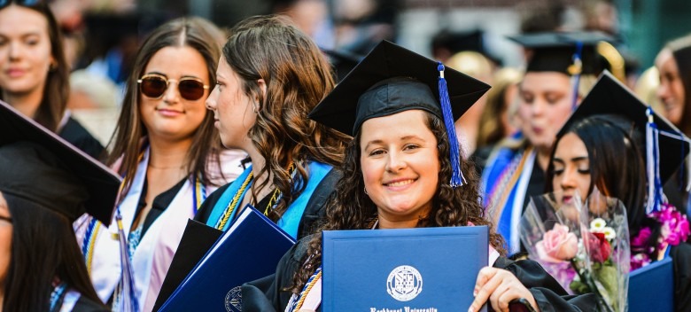 A 2025 Rockhurst University graduate shows her diploma while in a crowd of fellow students