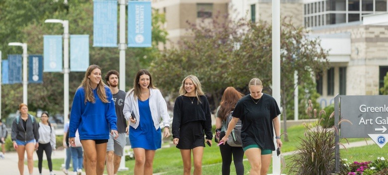 A group of students walk to class with campus imagery behind them 