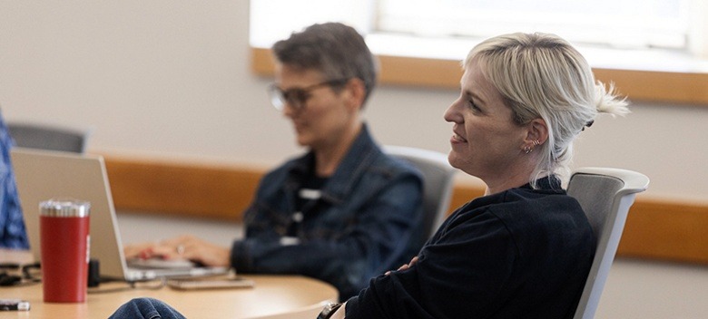 A woman sits back in her chair at a table while in an EMBA class