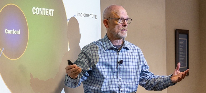 An EMBA professor speaks in front of a slide talking about content and context