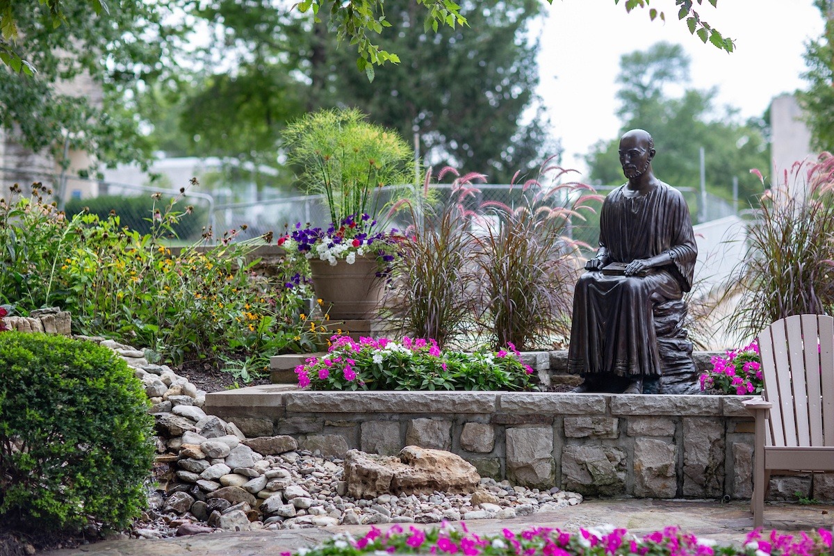 Statue of Saint Ignatius next to small waterfall and flower beds
