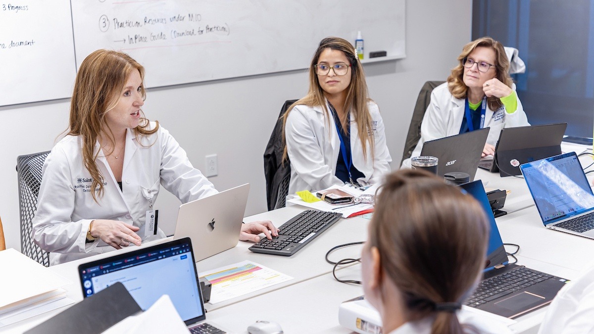 Healthcare administrators talk at a table with open laptops 