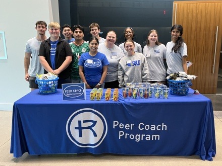Group photo of students participating in the Rockhurst University Peer Coach Program, standing behind a table