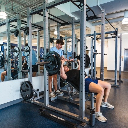 A student prepares to bench press weights in the Magis Activity Center (MAC) as a friend spots him