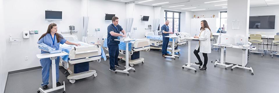 Nursing students stand beside hospital beds before an instructor