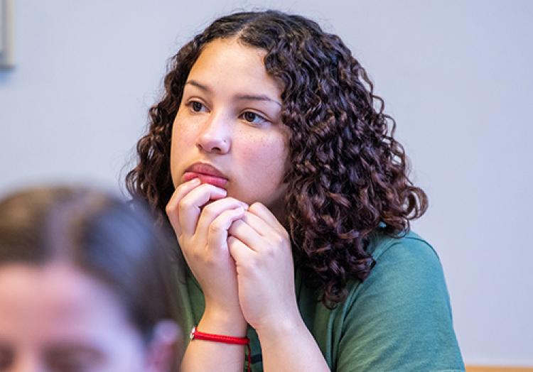 Close up of female student, hands on chin, in a classroom focused on the front of the room