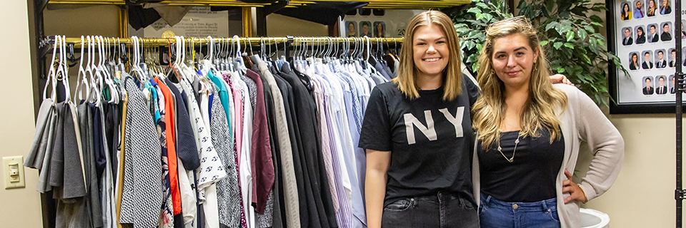 Two students stand in front of clothing rack